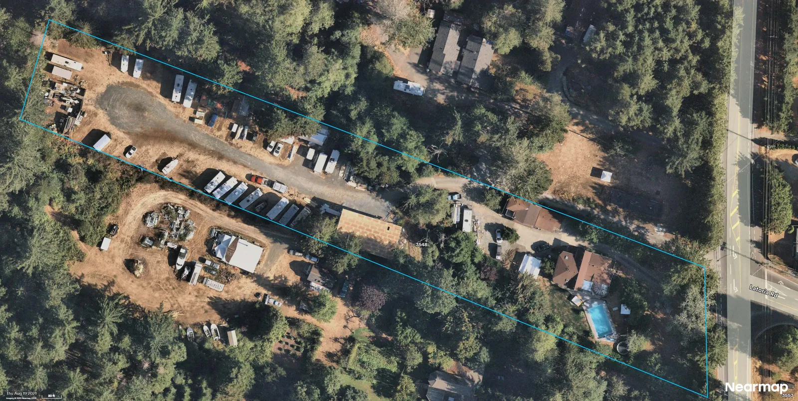 Aerial photograph showing the parcel outlined in blue with trailers/RVs clustered along the central drive; residence and pool near the right edge adjacent to Latoria Rd; trees casting shadows over portions of the site.