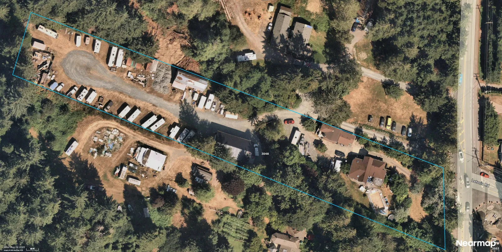Aerial photograph showing the parcel outlined in blue with numerous trailers/RVs and equipment in the western portion and along the central drive; residence and pool near Latoria Rd on the east; surrounding vegetation and cleared areas visible.