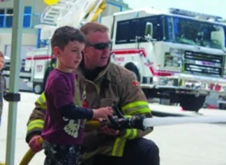 Volunteer firefighter Steve Clarke shows four-year-old Michael Paquette how to use a fire hose during Colwood Fire Rescue’s annual open house (Black Press file photo).